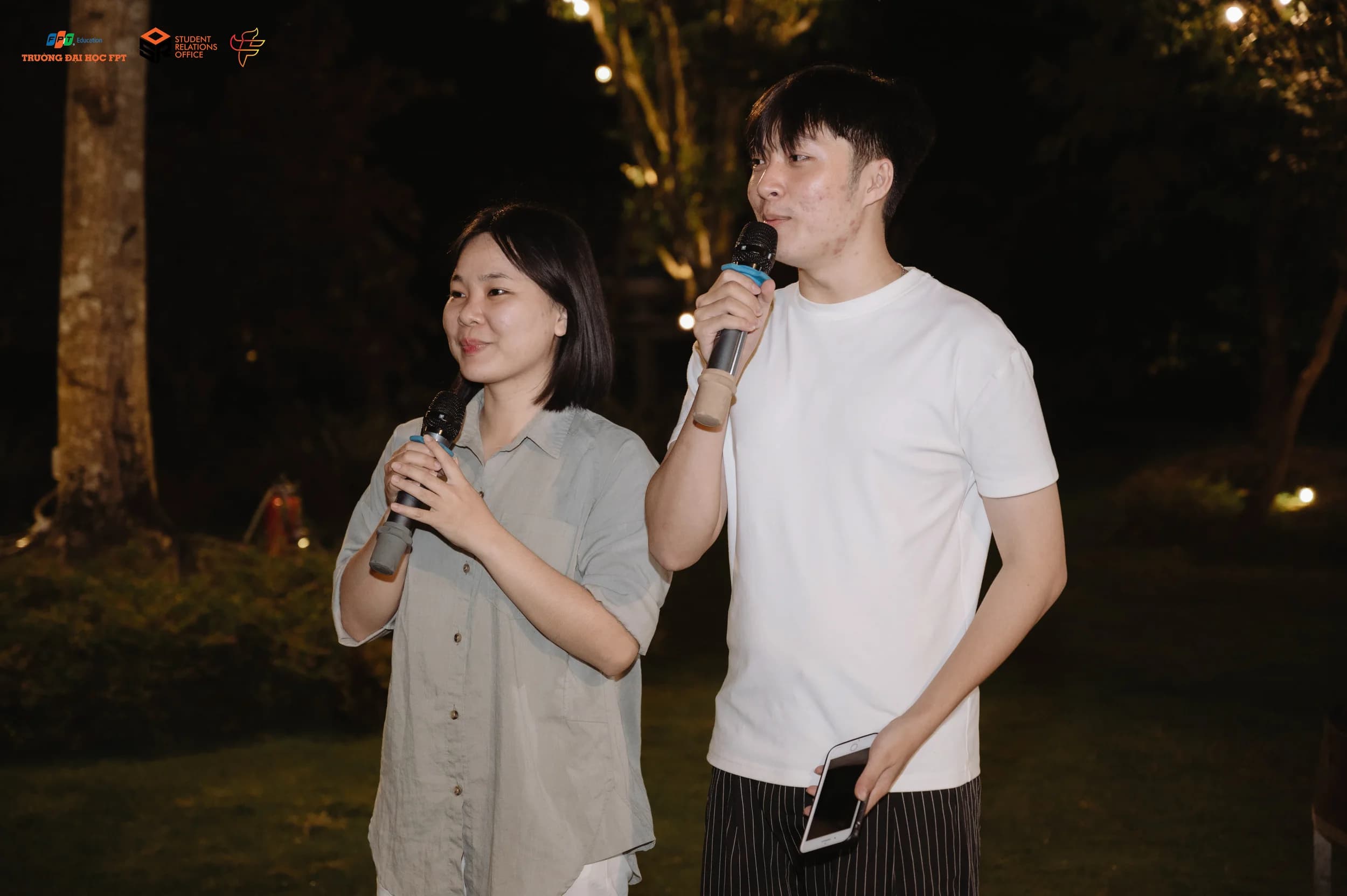 Hai người dẫn chương trình cầm micro tại một sự kiện ngoài trời