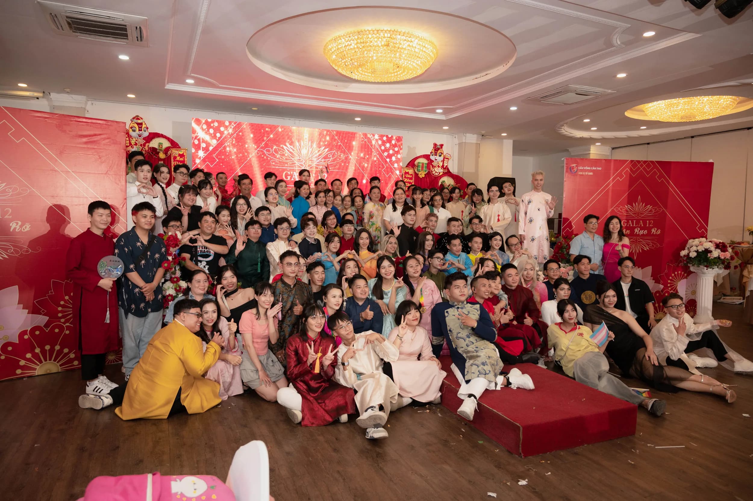 Đông đảo khách mời tập trung chụp ảnh kỷ niệm trong một sự kiện mừng năm mới tại sảnh tiệc trang trí rực rỡ sắc đỏ.