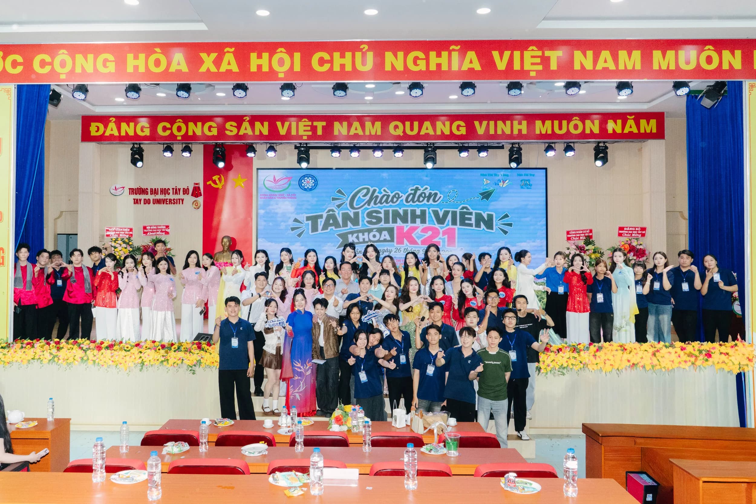 Nhóm người chụp ảnh tập thể trước màn hình Chào đón tân sinh viên khóa K21 tại Đại học Tây Đô